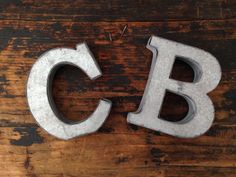 two metal letters sitting on top of a wooden floor next to each other, with the letter c and b cut out