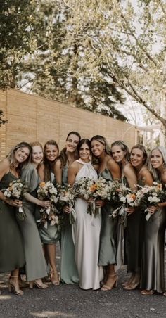 a group of women standing next to each other wearing dresses and holding bouquets in their hands