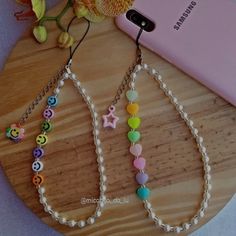 two cell phones are sitting next to each other on a wooden table with beads and charms