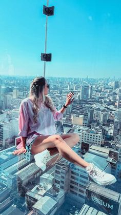 a woman sitting on top of a tall building with her legs spread out and hands in the air