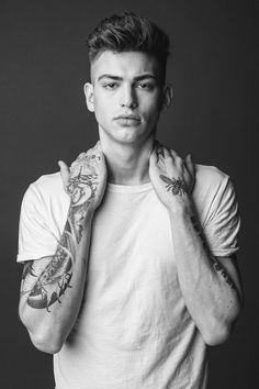 a young man with tattoos on his arms and shoulder is posing for a black and white photo