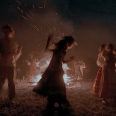 a group of people standing around a fire pit at night with their arms in the air