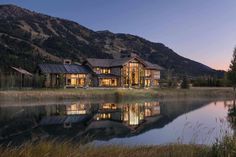 a large house sitting on top of a lush green hillside next to a lake at night