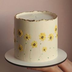 a hand holding a white cake with yellow flowers on it