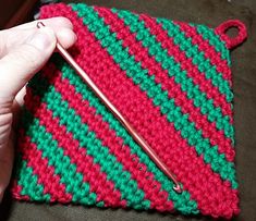 a hand holding a crocheted red and green piece of cloth with a knitting needle in it