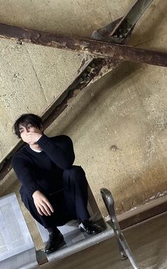 a woman sitting on top of a metal bench next to a brick wall and exposed ceiling