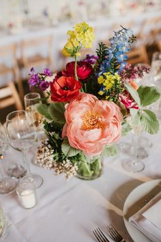 a vase filled with flowers on top of a table next to wine glasses and silverware