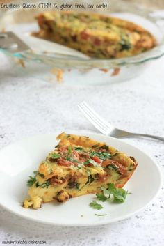 a slice of quiche on a white plate with a fork and glass dish in the background