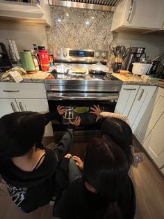 three women are looking into an oven in the kitchen