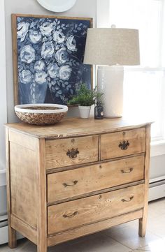 a wooden dresser sitting in front of a window with a lamp on top of it