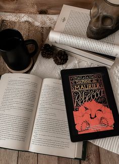 an open book sitting on top of a table next to two coffee mugs and books