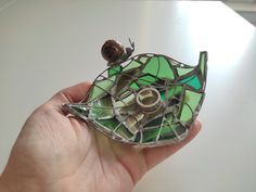 a hand holding a small stained glass piece with a snail on it's back