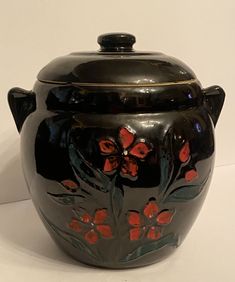 a large black vase with red flowers painted on the front and sides, sitting on a white surface