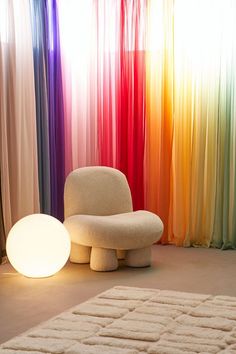 a white chair sitting on top of a carpet next to a rainbow colored curtained wall