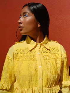 a woman with her eyes closed standing in front of a red wall wearing a yellow shirt