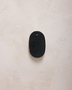 a black object on a white wall with a hole in it's center that is shaped like a dog tag