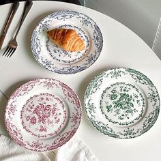 three plates with croissants on them are sitting on a table next to utensils