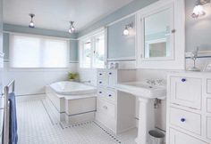 a white bathroom with blue walls and flooring is pictured in this image, there are three lights above the bathtub