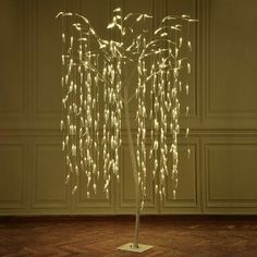 a lighted tree in a room with wood flooring and white walls, decorated with branches