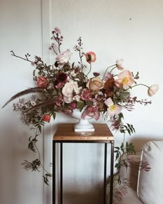 an arrangement of flowers in a white vase on a small wooden table next to a couch