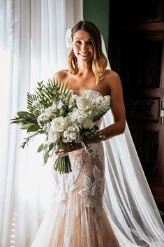 a beautiful woman in a wedding dress holding a bouquet of white flowers and greenery