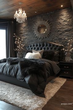 a bedroom with stone walls, black bedding and chandelier hanging from the ceiling