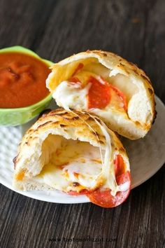 two pieces of pizza on a plate next to a small bowl of tomato sauce and dipping sauce