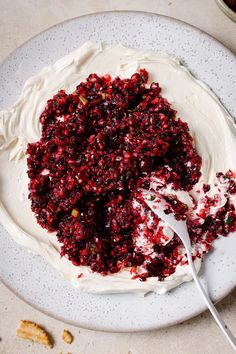 a white plate topped with whipped cream and cranberry topping next to a spoon