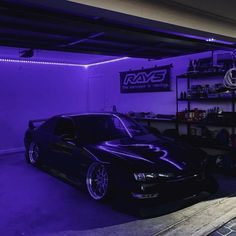 a black car parked in a garage with purple lighting on the walls and below it