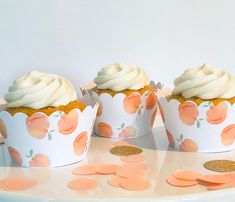 three cupcakes with white frosting and peaches on them sitting on a table