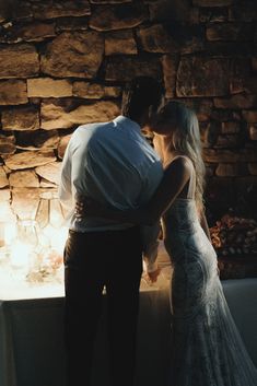 a man and woman standing next to each other in front of a stone wall at night