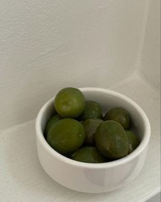 a white bowl filled with green olives on top of a counter