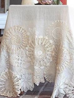 a table topped with a white doily covered table cloth next to a vase filled with flowers