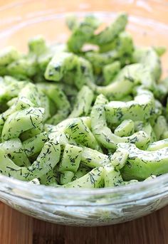 a glass bowl filled with cucumbers on top of a wooden table