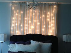 a bed with white pillows and some lights on the wall behind it in front of a window