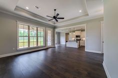 an empty living room with wood flooring and ceiling fan in the middle of it