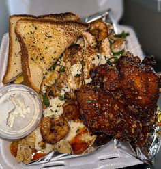 a tray filled with meat, bread and other food on top of foil wrappers