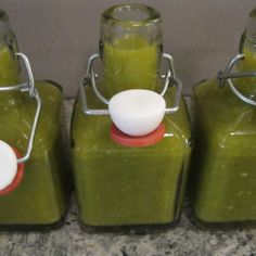 three jars filled with green smoothie sitting on top of a counter