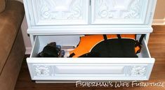 a white armoire with an orange and black bag in the bottom drawer next to a brown couch