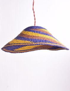 a woven hat hanging from a string on a white wall with a red cord in the foreground