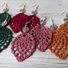 three pairs of crocheted earrings are shown in different colors and designs on a white wooden surface