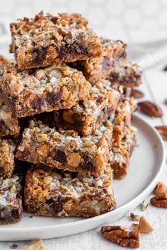 a stack of granola bars on a white plate with pecans around the edge