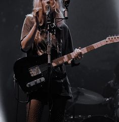 a woman singing into a microphone while holding a guitar