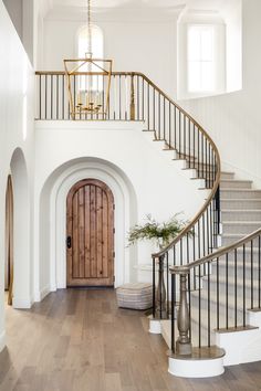 a staircase leading up to a wooden door in a white house with wood floors and railings