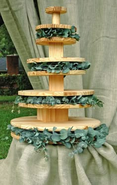 a three tiered cake stand with greenery on the bottom and green leaves on top