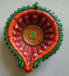 an orange and green decorative bowl sitting on top of a white table next to a wall