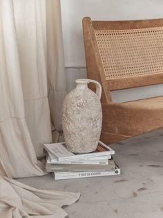 a white vase sitting on top of three books next to a wooden bench and chair