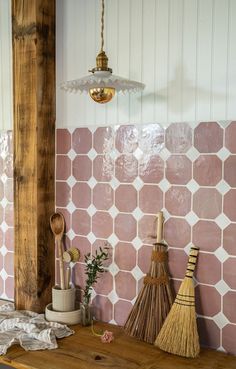 a wooden table topped with brooms next to a wall covered in pink and white tiles