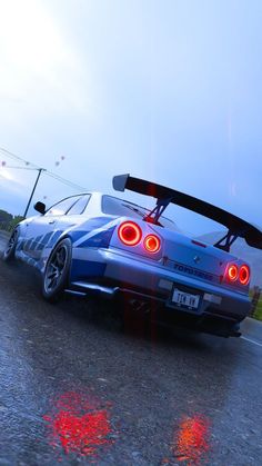 a blue sports car with its lights on driving down the road in the evening time