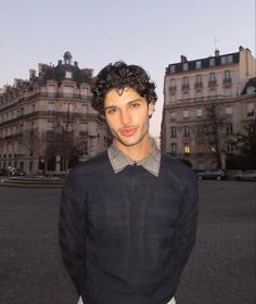 a man is standing in front of some buildings and looking at the camera with a serious look on his face